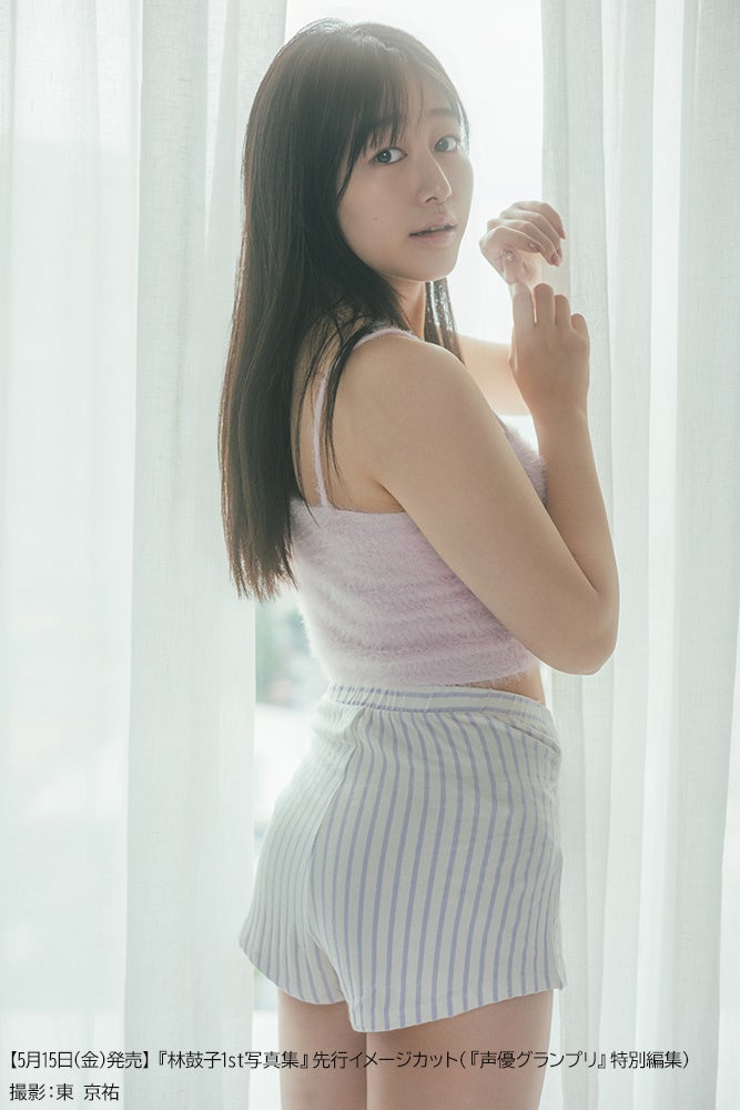 薄い服を着た女性が室内でカーテンの前に立つ様子