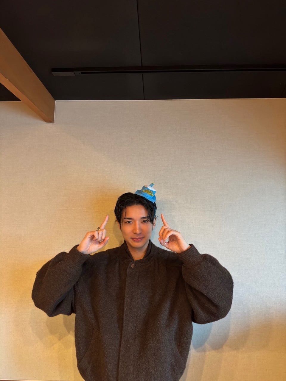 茶色のコートを着た男性が笑顔でポーズ